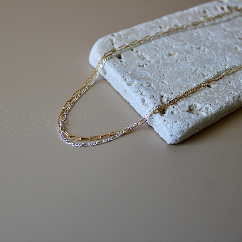May include: A gold and silver chain necklace. The necklace is made of two chains, one gold and one silver, that are linked together.