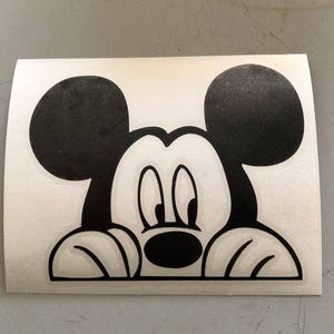 Può includere: Adesivo in bianco e nero di Topolino che sbircia da dietro una superficie bianca. Topolino guarda a destra con le orecchie dritte.