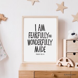 Puede incluir: Un estampado enmarcado con el texto "I AM FEARFULLY AND WONDERFULLY MADE" en negro, con "PSALM 139:14" debajo. El estampado está en un marco de madera clara, sobre una superficie de madera con juguetes de madera y decoraciones de estrellas.