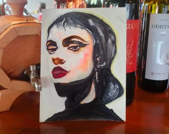 May include: A painting of a woman's face with dark hair and a black turtleneck. The painting is on a white canvas and is propped up against a wooden surface. There are three bottles of wine in the background.