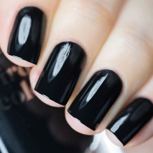 May include: Close-up of a hand with polished black fingernails. The nails are a glossy, solid black color, reflecting light. The image focuses on the nails, showcasing their shape and the smooth, even application of the nail polish.