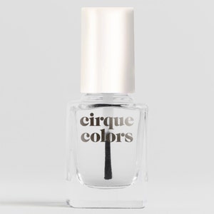 May include: A clear glass bottle of nail polish with a white cap. The bottle has a black brush and a label that says "cirque colors".
