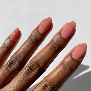 Puede incluir: Primer plano de una mano con cuatro dedos pintados con un esmalte de u&ntilde;as rosa claro. Las u&ntilde;as son de forma ovalada y el esmalte es brillante.