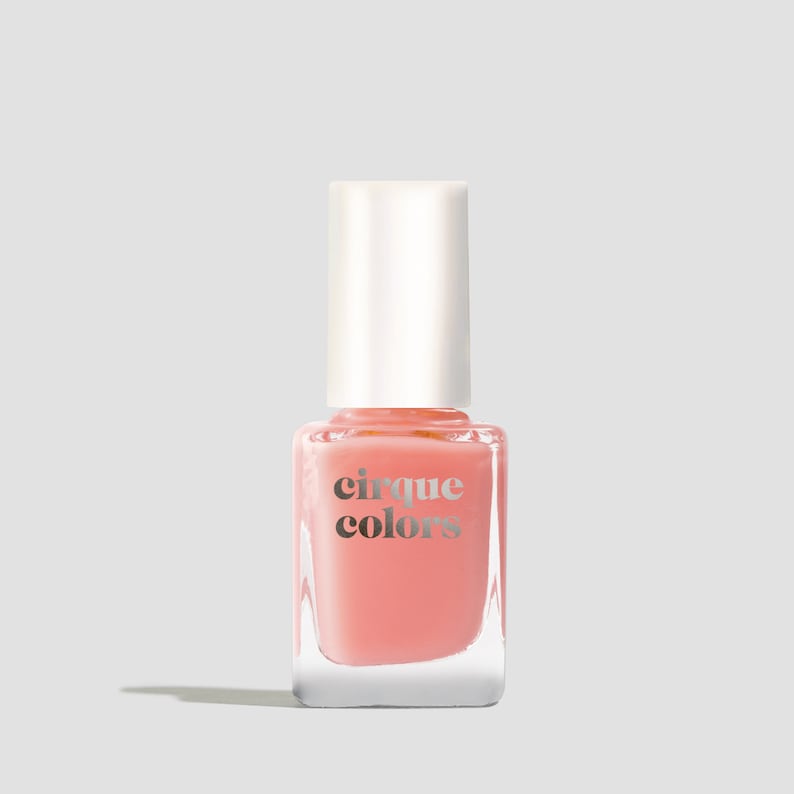 Puede incluir: Una botella de vidrio transparente de esmalte de u&ntilde;as rosa con una tapa blanca. La botella tiene el texto "cirque colors" impreso en la parte delantera.