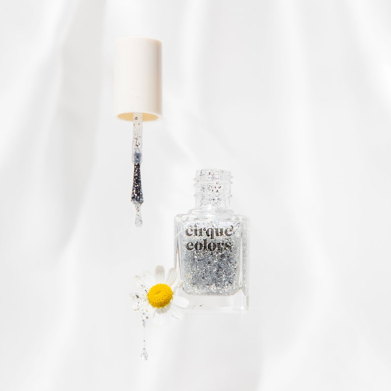 May include: A clear bottle of silver glitter nail polish with a black cap and a silver brush. The bottle is labelled "cirque colors".