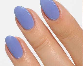 May include: Close-up of three fingernails painted with a light periwinkle blue nail polish.