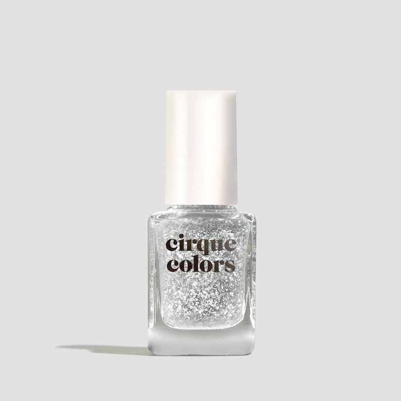 May include: A clear glass bottle of silver glitter nail polish with a white cap. The bottle has the text "cirque colors" printed on the front.