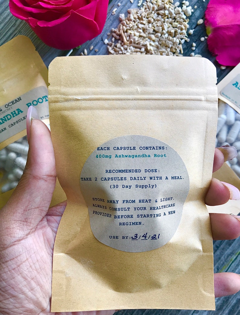 Op de afbeelding: Een bruine papieren zak met een wit label waarop staat: "EACH CAPSULE CONTAINS: 400mg Ashwagandha Root RECOMMENDED DOSE: TAKE 2 CAPSULES DAILY WITH A MEAL. (30 Day Supply) STORE AWAY FROM HEAT & LIGHT. ALWAYS CONSULT YOUR HEALTHCARE PROVIDER BEFORE STARTING A NEW REGIMEN. USE BY: 3/4/21"