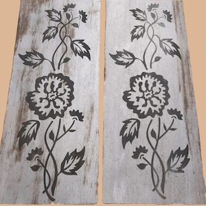 May include: Two rectangular wooden panels with a distressed white finish. Each panel features a dark gray floral design with a large flower at the bottom and a winding stem with leaves and smaller flowers.