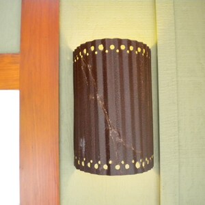 May include: A brown metal outdoor light fixture with a corrugated design and a row of small holes around the top and bottom edges.