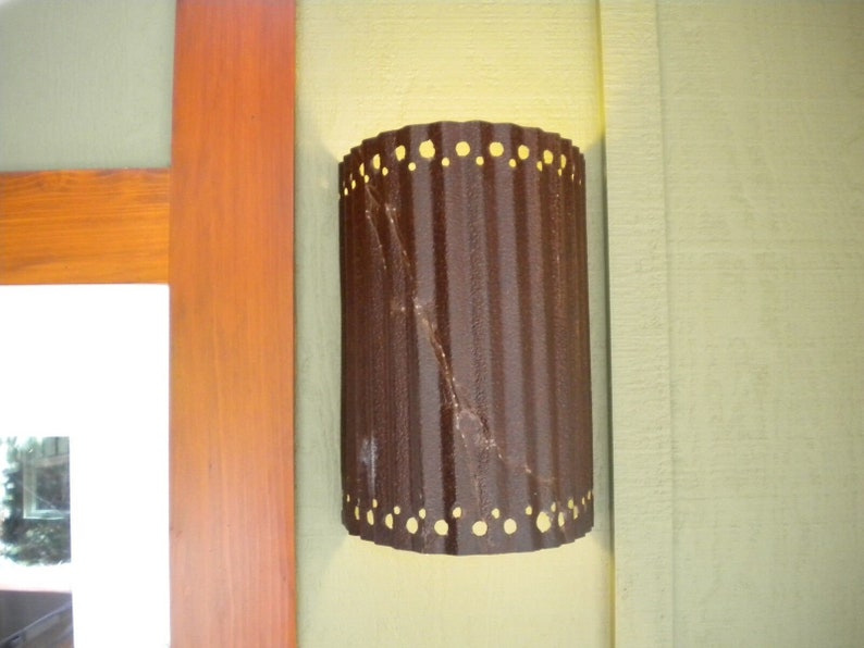 May include: A brown metal outdoor light fixture with a corrugated design and a row of small holes around the top and bottom edges.