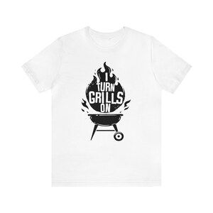 May include: White t-shirt with a black graphic of a grill and flames. The text "I turn grills on" is printed on the graphic.
