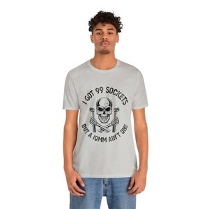 May include: A light gray t-shirt with a skull and crossbones graphic. The text on the shirt reads "I got 99 sockets but a 10mm ain't one".