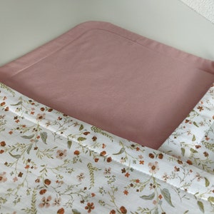 K&ouml;nnte beinhalten: Eine rosa-wei&szlig;e Wickelunterlage mit Blumenmuster. Die Unterlage ist in der H&auml;lfte gefaltet, so dass die rosa Seite oben und die Blumenmusterseite unten sichtbar ist.