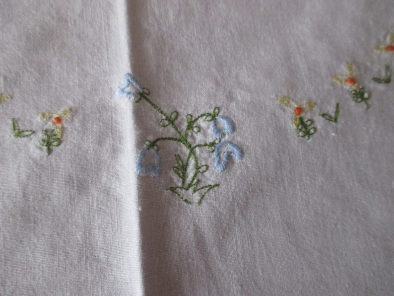 Puede incluir: Mantel de mesa de lino blanco con flores bordadas en azul y verde. Las flores est&aacute;n en un racimo y tienen un aspecto delicado y vintage.