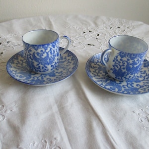 May include: Two blue and white porcelain teacups and saucers with a floral design. The cups have a small handle and the saucers have a scalloped edge.
