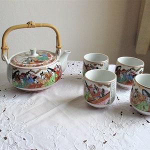 Könnte beinhalten: Eine weiße Porzellan-Teekanne mit einem Bambusgriff und Blumendesigns. Die Teekanne ist von vier passenden Teetassen mit ähnlichen Blumendesigns umgeben.