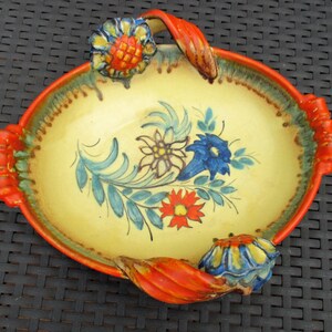 Puede incluir: Un plato de servir de cer&aacute;mica amarillo con asas naranjas y dise&ntilde;os florales en azul, rojo y verde. El plato tiene un borde festoneado y es de forma ovalada.