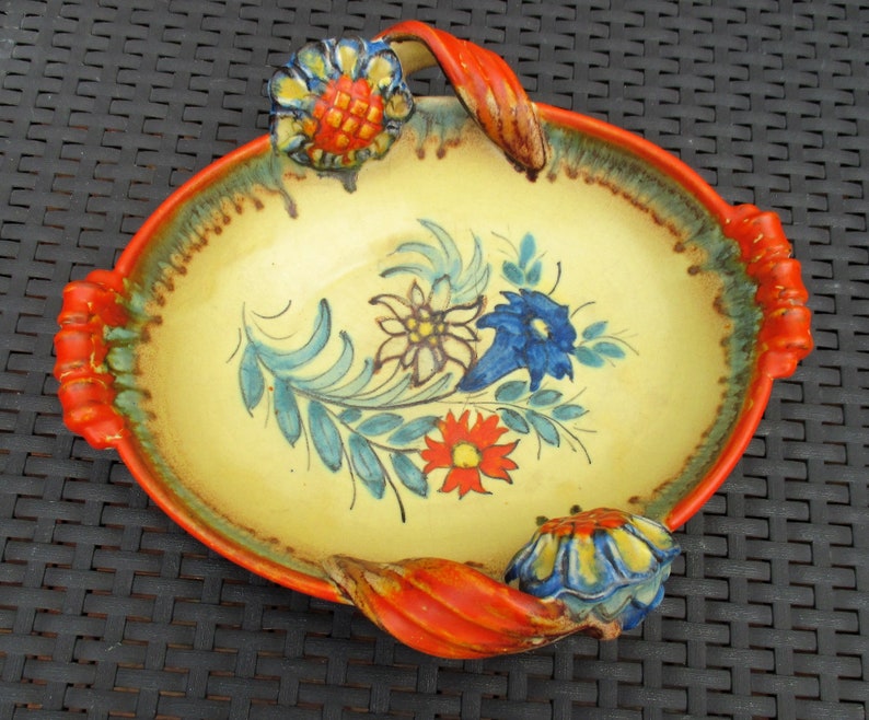 Puede incluir: Un plato de servir de cer&aacute;mica amarillo con asas naranjas y dise&ntilde;os florales en azul, rojo y verde. El plato tiene un borde festoneado y es de forma ovalada.