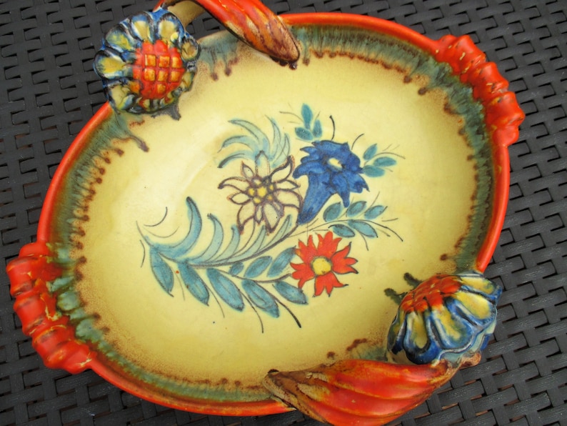 Puede incluir: Un plato de servir de cer&aacute;mica amarillo con dos asas naranjas y dise&ntilde;os florales en azul, rojo y blanco. El plato tiene un aspecto r&uacute;stico y pintado a mano.