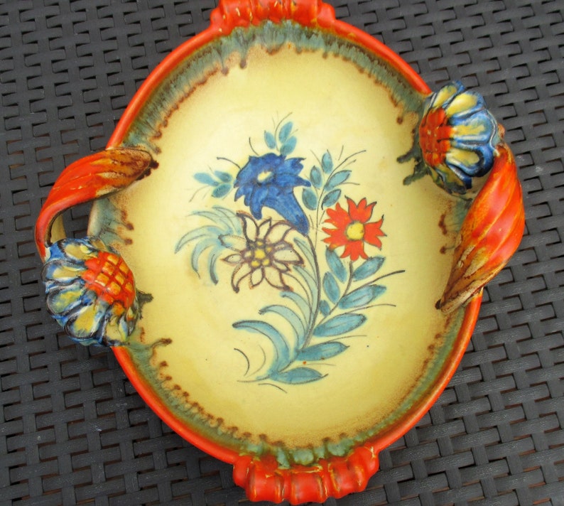 Puede incluir: Un plato de servir de cer&aacute;mica amarillo con asas naranjas y un dise&ntilde;o floral pintado en azul, rojo y verde.