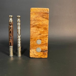 Può includere: Due vaporizzatori con finiture in acciaio inossidabile e legno, accanto a una scatola di legno con due magneti argentati. Un vaporizzatore ha un motivo a venature marroni e nere. L'altro è argentato con un design strutturato. La scatola è in legno marrone chiaro.