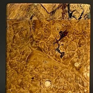 Op de afbeelding: Een close-up van een houten doos met een uniek burl-houten patroon. Het hout heeft een rijke bruine kleur met swirls en knopen.