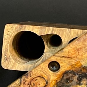 Op de afbeelding: Een houten doos met twee ronde gaten en een kleiner gat aan de zijkant. De doos is gemaakt van lichtbruin hout met een donkerbruine nerf. De doos is open en de binnenkant is zichtbaar.