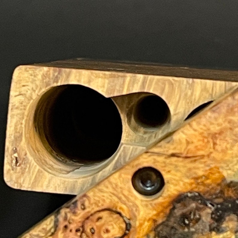 Op de afbeelding: Een houten doos met twee ronde gaten en een kleiner gat aan de zijkant. De doos is gemaakt van lichtbruin hout met een donkerbruine nerf. De doos is open en de binnenkant is zichtbaar.