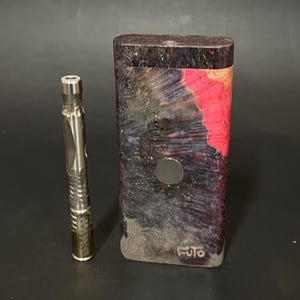 May include: A black and red wooden box with a silver metal circle on the front. The box has the word "FUTO" printed on the bottom. A silver metal tool with a textured surface is next to the box.