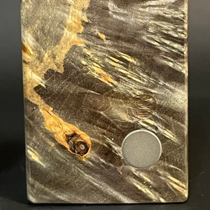 Op de afbeelding: Een close-up van een houten oppervlak met een uniek houtnerfpatroon. Het oppervlak is donkerbruin met lichtbruine strepen en een cirkelvormig grijs metalen accent.