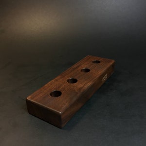 May include: A dark brown wooden stand with five circular holes, designed to hold items like paintbrushes or pencils. The stand has the word "F.U.T.S" engraved on the side.