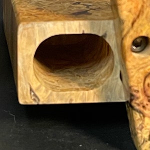 Op de afbeelding: Een houten doos met een natuurlijke houtnerf afwerking. De doos heeft een rechthoekige vorm met een afgeronde opening aan &eacute;&eacute;n kant. De doos is gemaakt van lichtbruin hout met donkerbruine strepen.