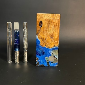May include: A wooden box with a blue and brown resin design. The box has a round, silver button on the front. Three glass and metal pipes are in front of the box.