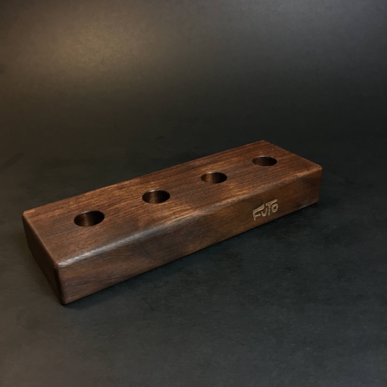 May include: A dark brown wooden stand with five holes for holding items. The stand is engraved with the word "FUTO".