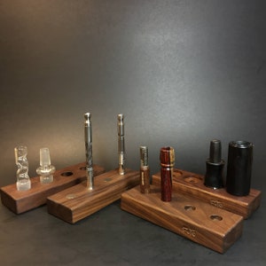 May include: A set of six wooden stands with various smoking accessories, including glass pipes, metal tools, and wooden pipes. The stands are made of dark wood and have a natural finish. The stands are labelled with the word "FOTO".