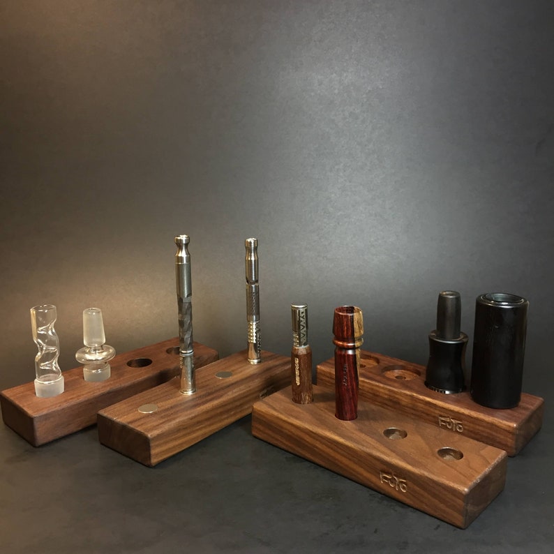 May include: A set of six wooden stands with various smoking accessories, including glass pipes, metal tools, and wooden pipes. The stands are made of dark wood and have a natural finish. The stands are labelled with the word "FOTO".