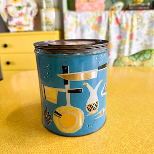 Puede incluir: Contenedor de metal turquesa vintage con un diseño geométrico dorado y negro. El contenedor tiene una tapa marrón oscuro y es de forma cilíndrica. El diseño incluye formas que se asemejan a utensilios de cocina.