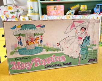 Puede incluir: Caja de juego vintage de Walt Disney's Mary Poppins Carousel. La caja presenta ilustraciones de un carrusel y Mary Poppins con un paraguas rosa. La caja es beige con texto y gráficos verdes y rosas. Un juego para niños y niñas de 5 a 10 años.