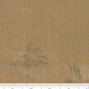 May include: A close-up of a brown fabric with a subtle textured pattern. The fabric has a slightly distressed look with a hint of green. The fabric is marked with a ruler in inches and the word "moda" appears twice.