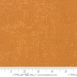 May include: A close-up of a fabric with a speckled pattern. The fabric is a light orange color with a subtle pattern of small white dots.
