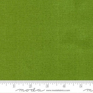 May include: A solid green fabric with a subtle textured pattern. The fabric is measured in inches with the text "moda" printed on the ruler.