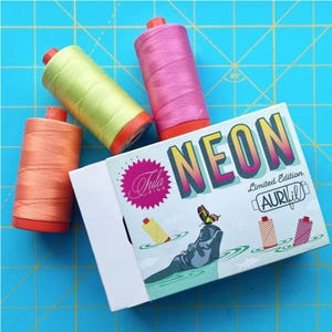May include: Three spools of neon colored thread in a box labeled "NEON Limited Edition AURIfil" with a hippopotamus and a butterfly on the front. The thread colors are pink, yellow, and orange.