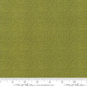 May include: A close-up of a green fabric with a subtle woven texture. The fabric has a slightly rough, linen-like feel. The fabric is shown with a ruler for scale.