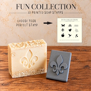 May include: A rectangular bar of beige soap topped with oats and embossed with a fleur-de-lis design, accompanied by a grey 3D printed soap stamp featuring the same fleur-de-lis motif. Text reads FUN COLLECTION 3D PRINTED SOAP STAMPS.