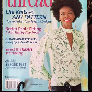 May include: A magazine cover for Threads magazine, featuring a woman wearing a light green blouse with a floral pattern. The magazine's title is in large pink letters. Text on the cover includes "Use Knits with Any Pattern" and "Better Pants Fitting."