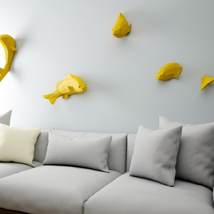 May include: A gray couch with three pillows and a white wall with five yellow origami fish decorations.