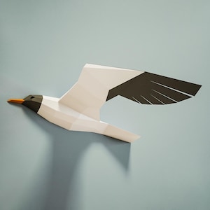 Könnte beinhalten: Eine weiße und schwarze Papier-Origami-Möwe mit orangefarbenem Schnabel im Flug vor einem hellblauen Hintergrund.