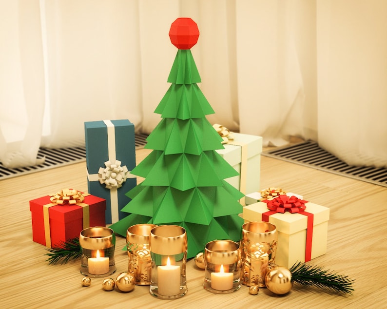 May include: A green paper origami Christmas tree with a red star on top, surrounded by wrapped gifts and gold candle holders with lit candles on a wooden surface.