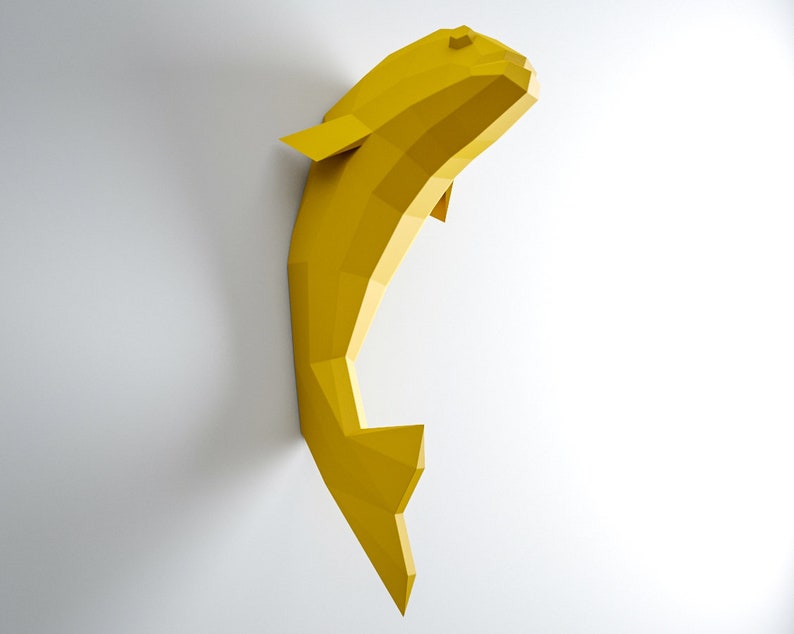 May include: A yellow origami fish sculpture, made of paper, is mounted on a white wall.